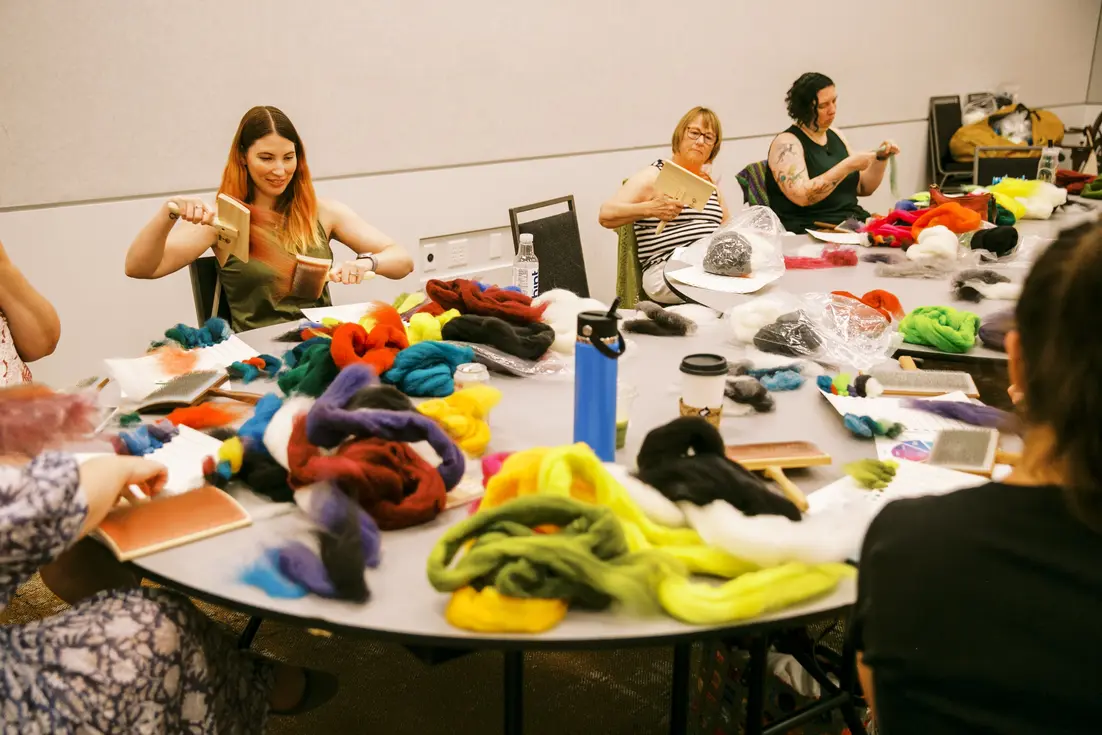 People examine and compare colorful yarn samples spread across a large workshop table.