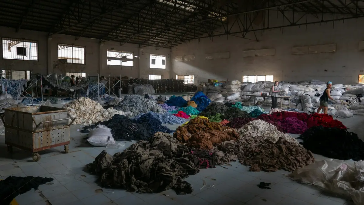 A large warehouse filled with piles of sorted textiles in various colors.
