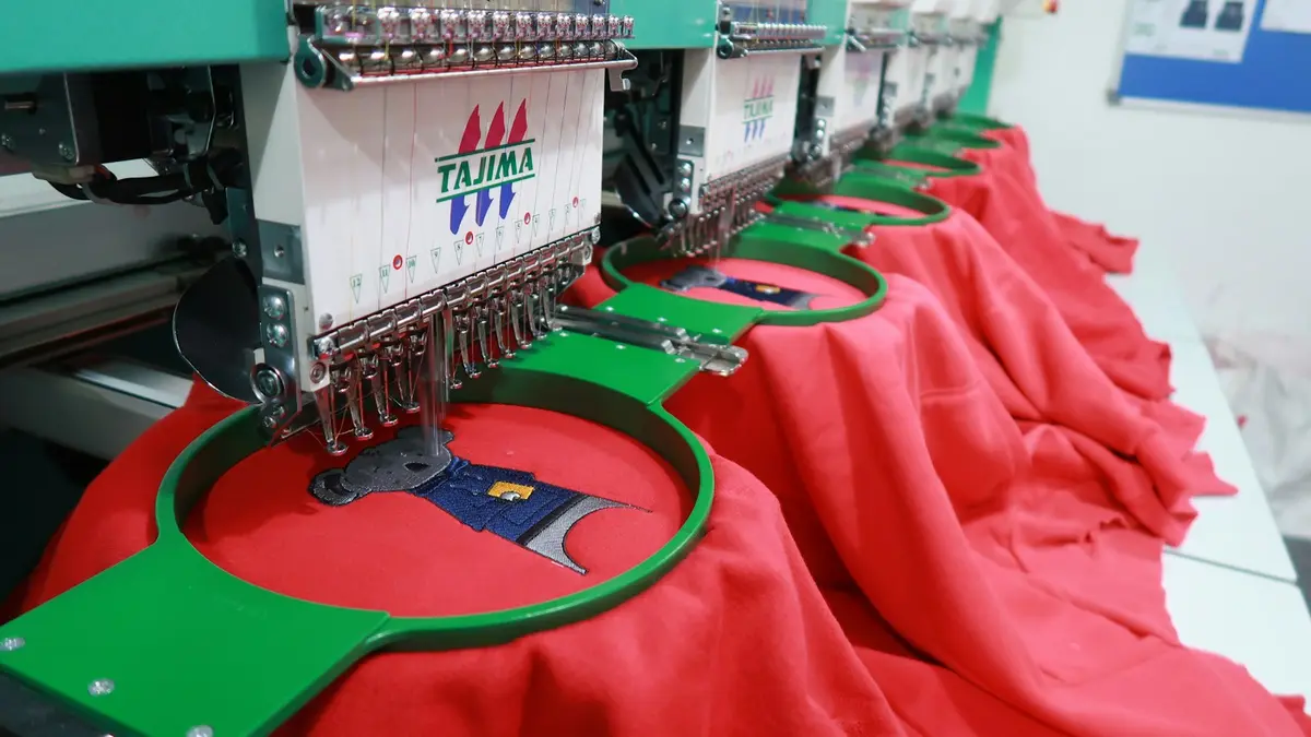 Several computerized embroidery machines set up with red fabric hooped for production.