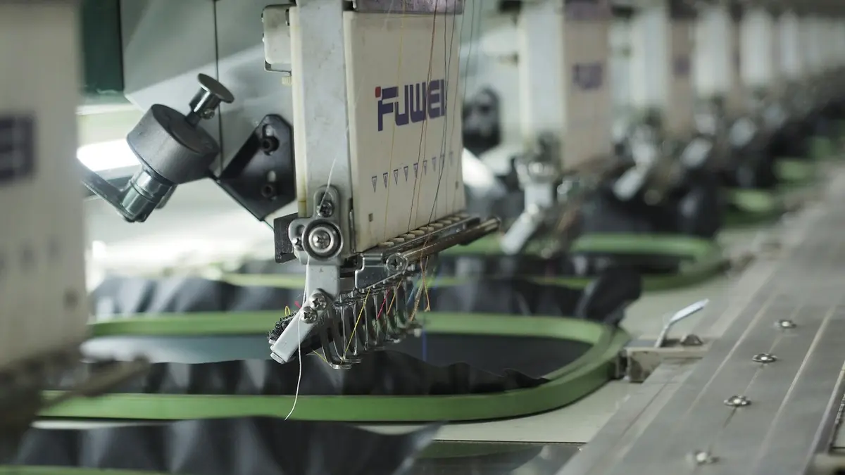 Multiple embroidery machine heads positioned over green fabric hoops in a production setup.