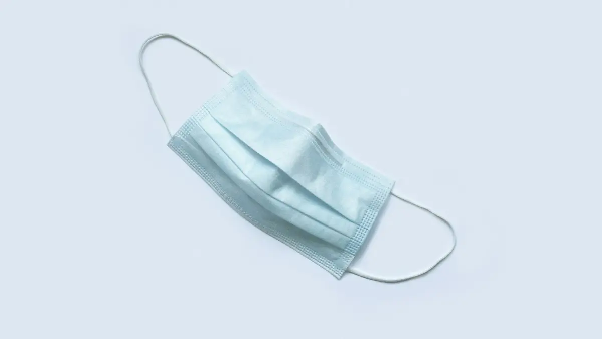 A light blue surgical mask with folded layers and ear loops on a light background.