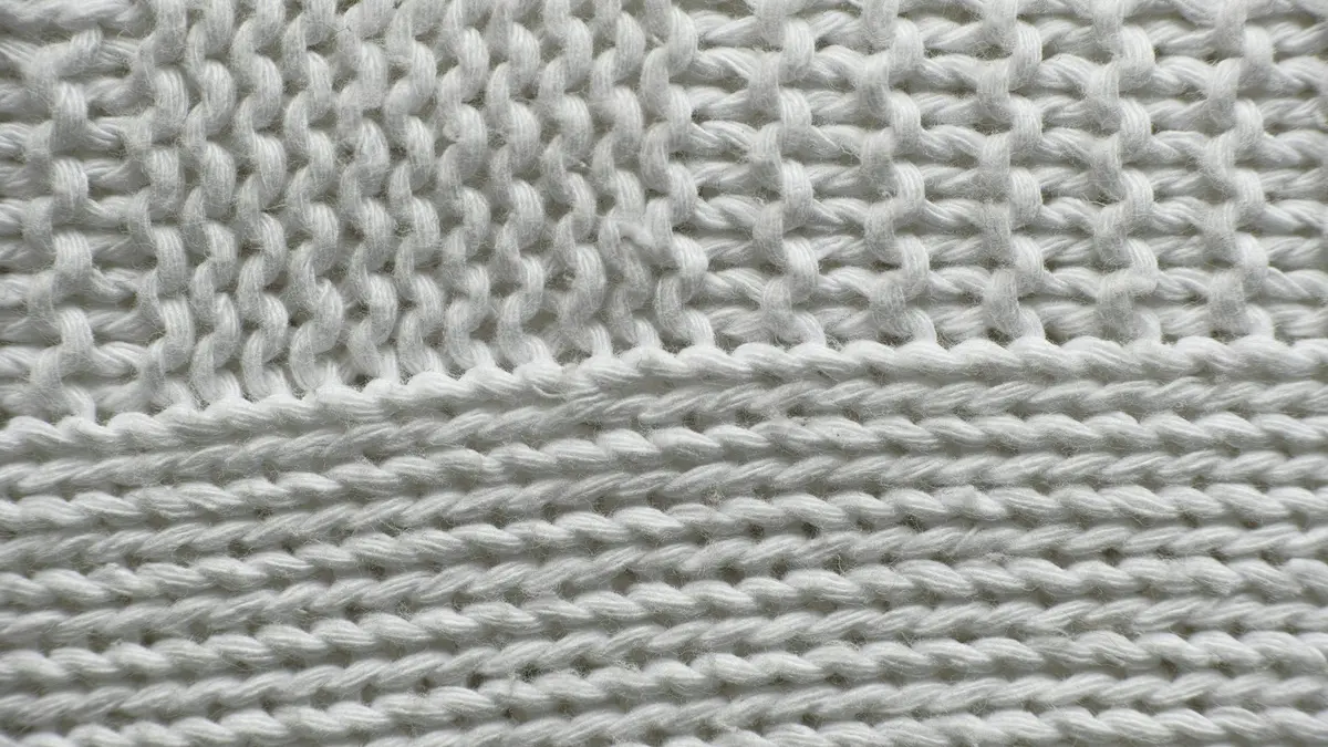 Close-up of white knitted textile showing varying stitch patterns and textures.