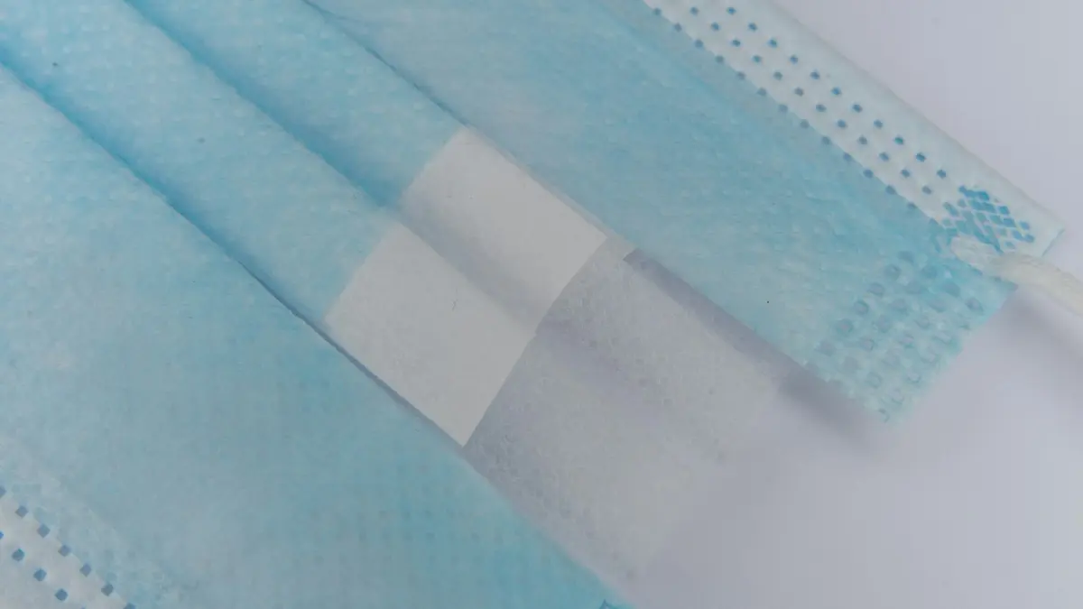 Layered blue nonwoven material used in disposable medical masks, showcasing texture and design features.