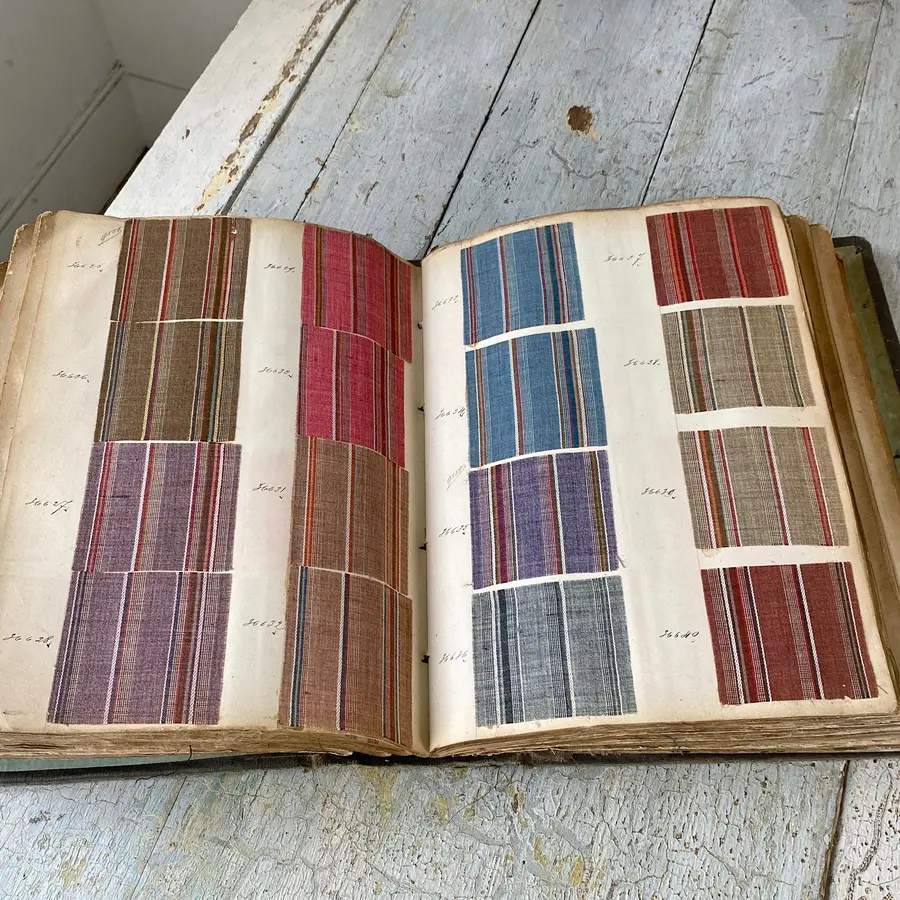 Open antique fabric sample book displaying rows of striped textile swatches on a weathered wooden table.
