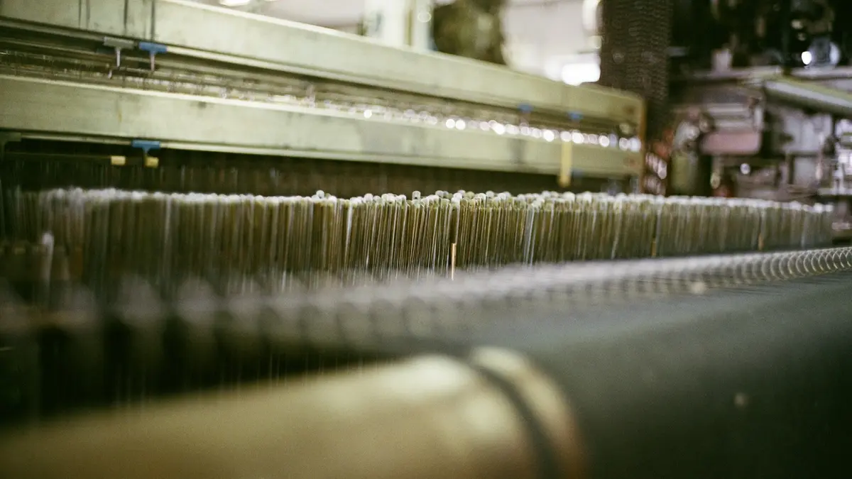 Close-up of weaving machine showing rows of yarn and spools in motion.
