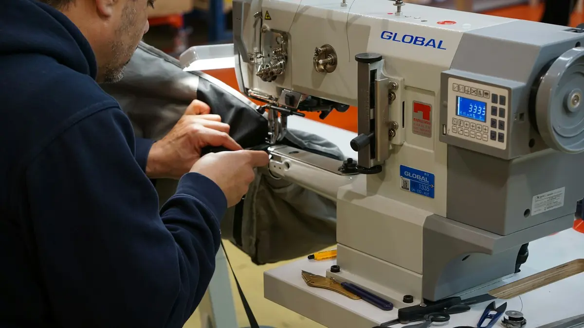 A person operates a sewing machine while working on a garment in a production setting.