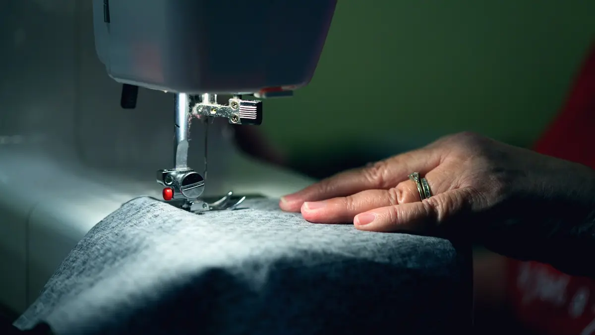 A close-up of a sewing machine with a hand guiding fabric underneath the needle.