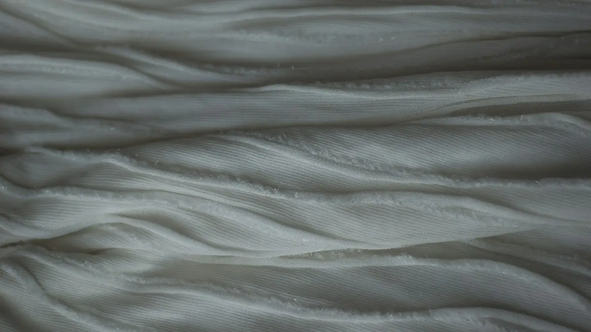 Flowing texture of layered, undulating white fabric with subtle sheen.