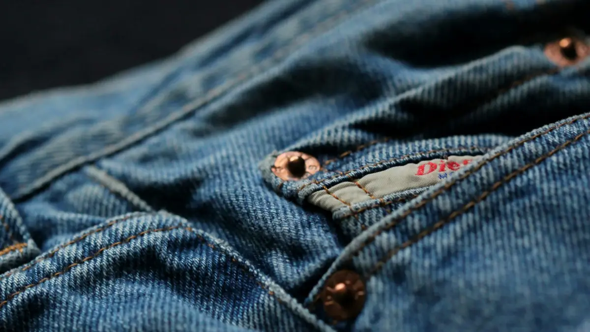 Close-up of denim fabric with rivets and a tag, showcasing a workwear style.