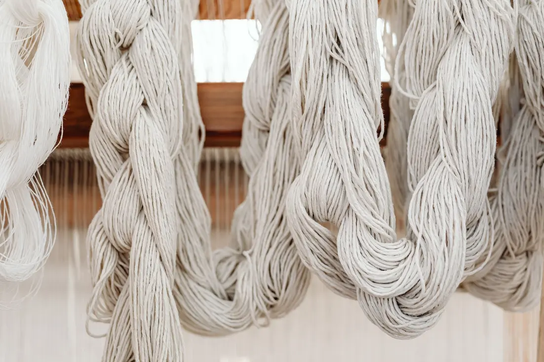 Hanks of light-colored yarn hanging in a textile studio.