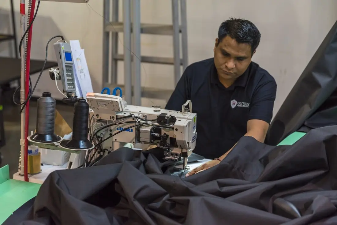 Worker operates an industrial sewing machine while guiding large pieces of black fabric.